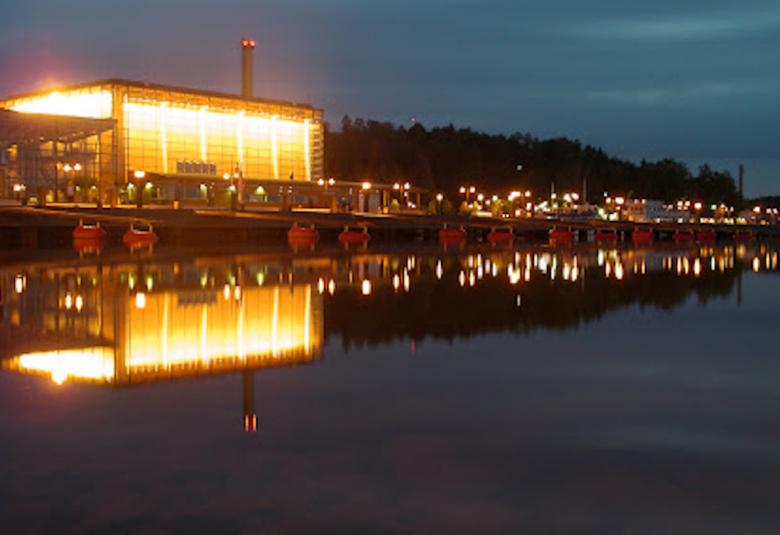 Kuvassa on Lahden Sibeliustalo iltavalaistuksessa ja kuva on otettu Vesijärven suunnasta.  Valot heijastuvat tummaan veteen.