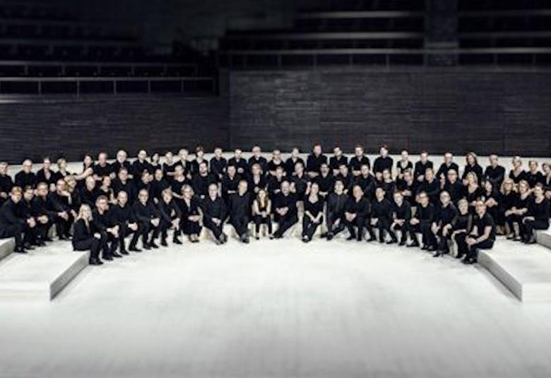 Kuvassa on RSO:n orkesteri istumassa orkesterikorokkeella. Orkesterin jäsenillä on musta-valkoiset tai mustat vaatteet. 