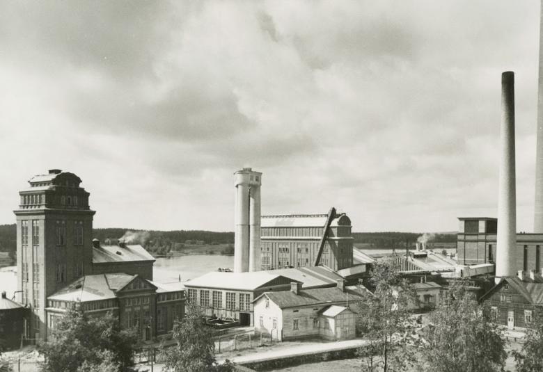 Kuvassa on Serlachiuksen tehdasmiljöö Mäntässä ja kuvassa näkyvät mm. tehtaan piiput. Kuva on musta-valkoinen.