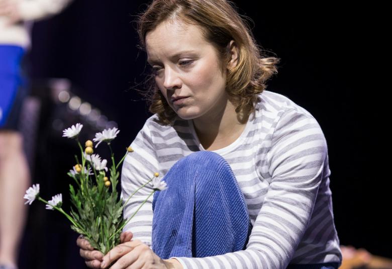 Kuvassa on Eleena Leeve, joka pitää kädessään valkoisia kukkia. 