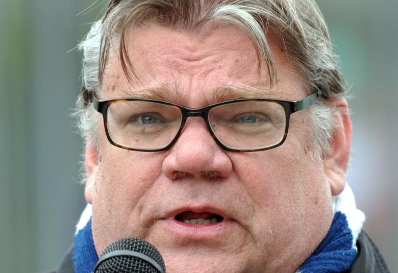 Kuvassa on Timo Soini puhumassa ulkona mikrofoni edessään. Kuva on kasvokuva.