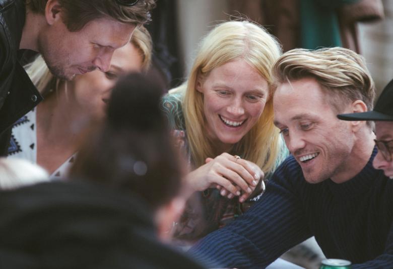 Kuvassa on Eero Milonoff, Emmi Parviainen, Laura Birn, Christian Hillborg ja Paavo Kinnunen. He ovat pöydän ääressä pelaamassa seurapeliä. 