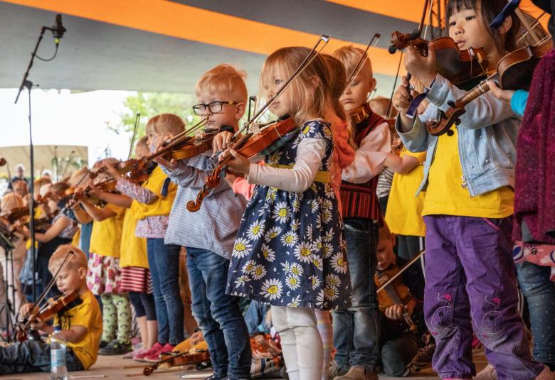 Kuvassa on pikkutyttöjä soittamassa viulua esiintymislavalla Kaustisilla.  Jokaisella on omat vaatteet esiintymisasuna.  