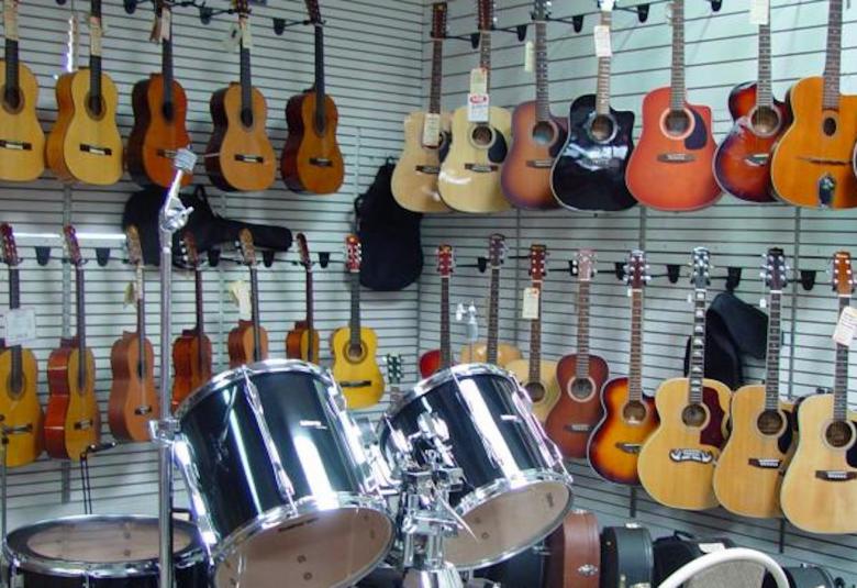 Kuvassa on seinälle ripustettu kitaroita useassa rivissä. Etualalla on rumpusarja.