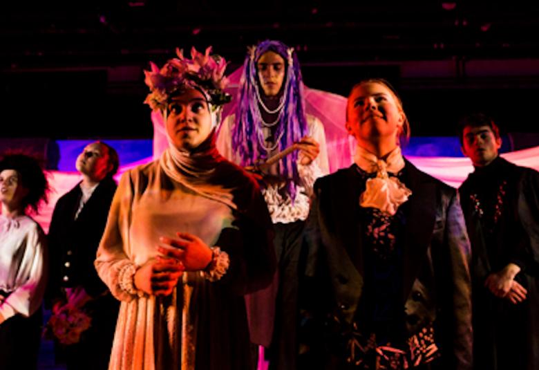 Kuvassa on nuoret näyttelijät ja edessä on pariskunta, joista naisella on huntu päässään.  Tausta on tumman sininen ja valaistus on tummahko.