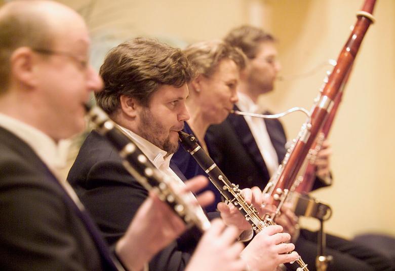 Kuvassa on sivuttain puupuhaltimien soittajia. Heitä on kuvassa neljä ja he ovat osana orkesteria.