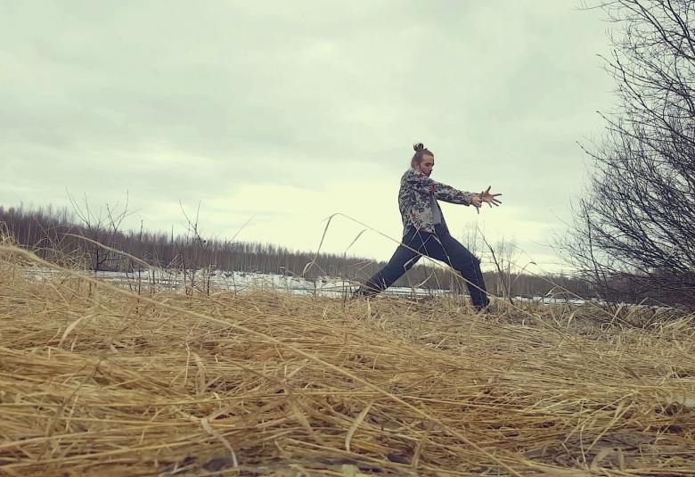 Kuvassa on tanssija Arvo Jean-Michael Saarinen tanssimassa rannalla, jossa on kuivunutta pitkää heinää.  