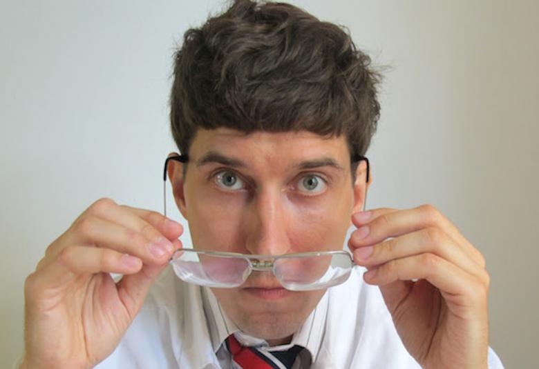 Kuvassa on Kasper Strömman ja hänellä on silmälasit kädessään.  Hänellä on lyhyet hiukset ja raidallinen värikäs kravatti. 