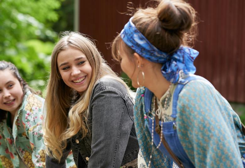 Kuvassa on kolme tyttöä keskustelemassa ulkona.  Keskimmäisenä on päähenkilö Emilia Skog.