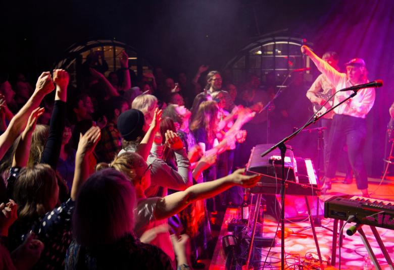 Kuvassa on G Livelab Tampereen konserttisalin konsertti, jossa yleisö kurkottaa kohti lavalla olevaa bändiä.  Kuvan valot ovat sinisiä ja punaisia.