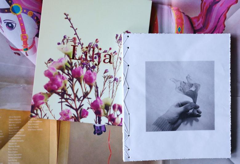 Kuvassa on kirjan Lilja kansi ja toisena on sisäsivu, jossa on on kuva kukasta. Taustalla on paperitaitoksia ja kuva pinkin punaisesta leikkihevosesta.