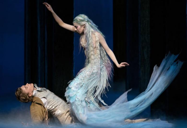 Kuvassa on kohtaus Kansallisoopperan esityksestä, jossa on miestanssija makuulla ja kalanpyrstöinen naistanssija on yläpuolella. 