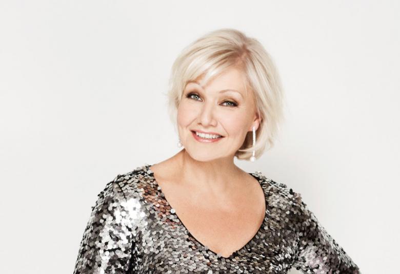 Kuvassa on Karita Mattilasta puolivartalokuva ja hän istuu.  Päällään hänellä on vaalea paljettipuku.