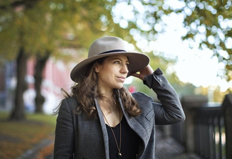 Kuvassa on Dalia Stasevska, joka on ulkona ja pitää kiinni lierihatusta.  Taustalla näkyy lehtipuita himmennettynä.