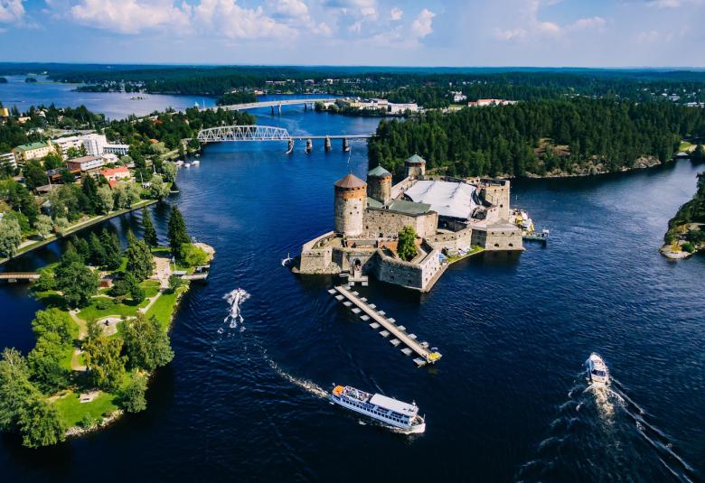 Kuvassa on Olavinlinna ja ympäröivää kaupunkia ylhäältä päin kuvattuna. Kuva on otettu aurinkoisena kesäpäivänä.