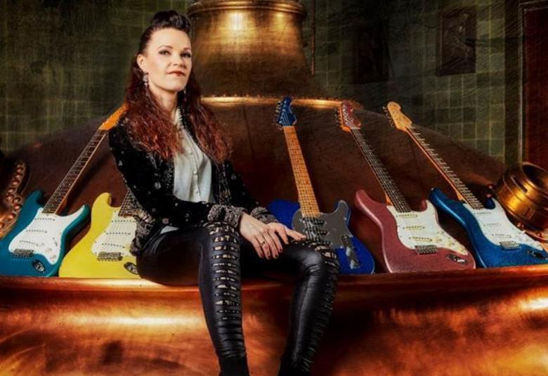 Kuvassa on Erja Lyytinen istumassa pyöreän isolla istuimella vieressään erilaisia ja värisiä kitaroita.