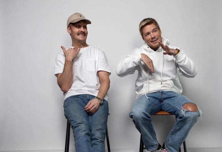 Kuvassa ovat Jare Brandin ja Ville Galle istumassa tuoleilla suuren valkokankaan edessä.