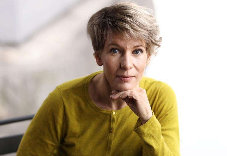 Kuvassa on Seija Ahava vihertävässä puserossa puolivartalokuvassa ja nojaamassa vasemmalla kädellän pöytään. 