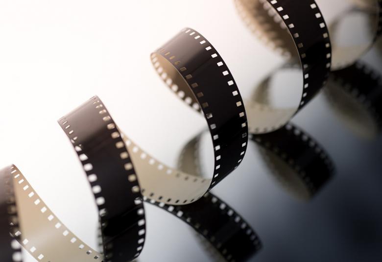 Kuvassa on valkoisella ja liukuvasti harmaalla pohjalla elokuvan filmiä, joka on viistosti kuvan läpi serpentiininä.