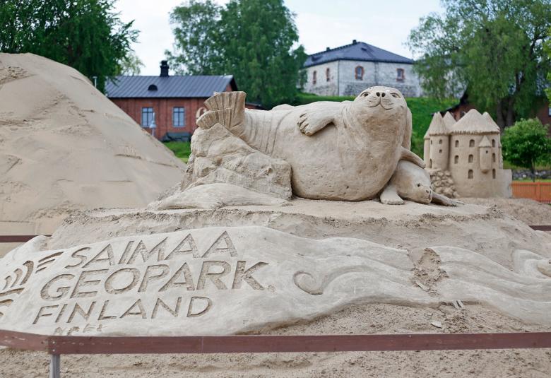 Kuvassa on Hiekkalinnan norppaveistos, jossa lukee Saimaa Geopark.