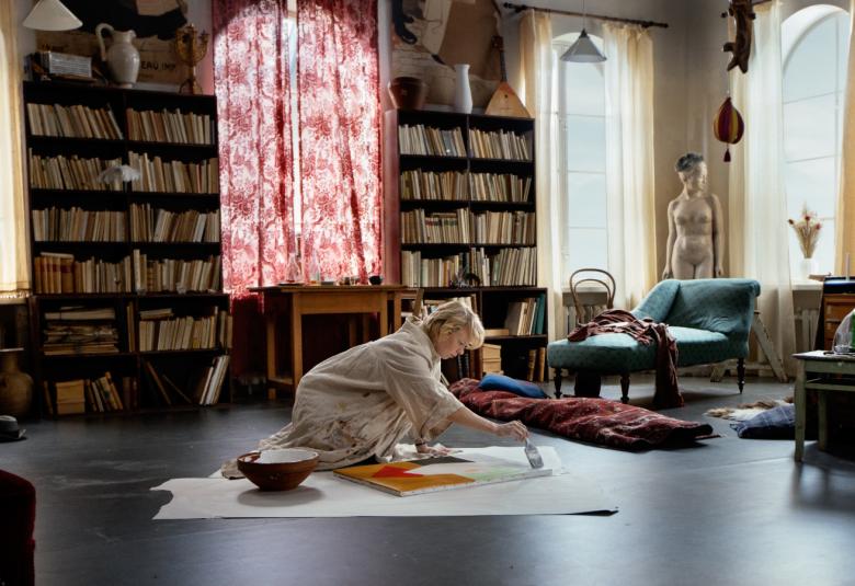 Kuvassa on Tove maalaamassa asuntonsa lattialla.  Huone on vanhassa talossa ja huone on korkea.