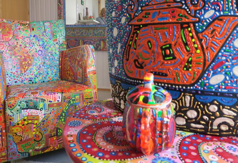 Kuvassa on värikkäästi ja pienillä yksityiskohdilla väritettyjä tuoleja ja muita arkisia esineitä.