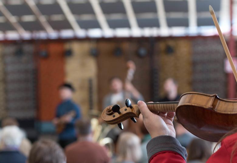 Kuvassa on Kaustisen festivaalijamit ja yleisön päitä.  Etualalla on ylös nostettu viulu.