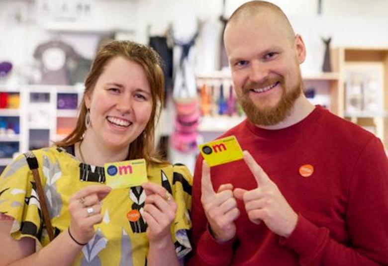 Kuvassa on vasemmalla nuorehko nainen kelta-kukallisessa mekossa ja mies punaisessa puserossa.  Molemmilla on kädessään museokortit.