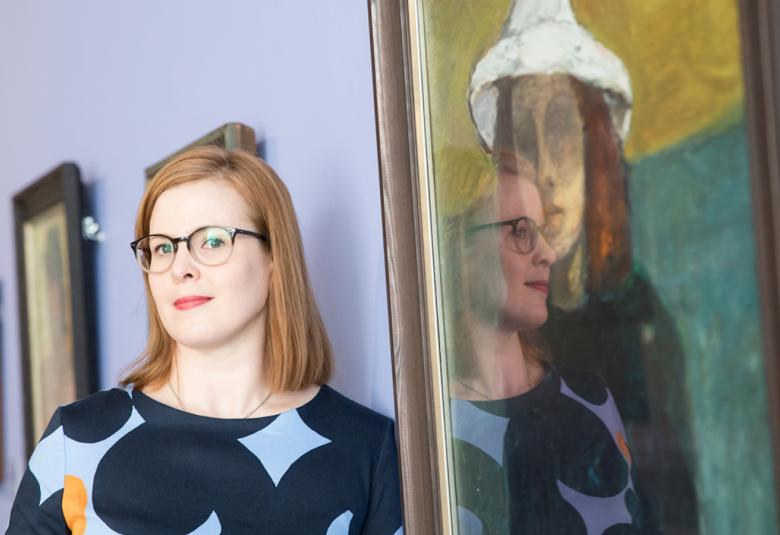 Kuvassa on Anu-Maarit Moilanen vieressään taulu, jossa on hatullinen nainen.