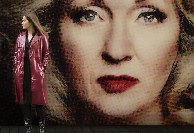 Kuvassa on isona taustakuvana Katariina Kaituen kuva ja edessä vasemmalla seisoo Anna Airola.