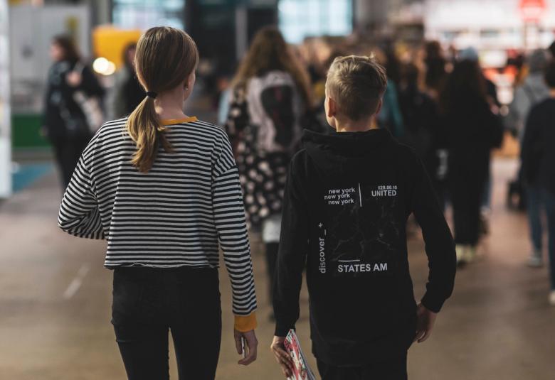 Kuvassa on oppilaita Helsingin Kirjamessuilla kävelemässä.  Kuva on oppilaista takaa päin.