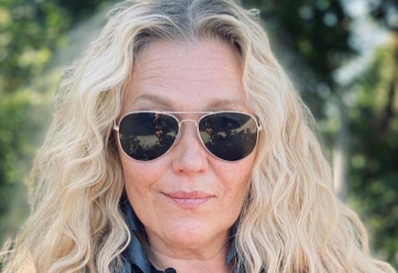 Kuvassa on Outi Mäenpää pitkissä vaaleissa hiuksissa ja aurinkkolasit silmillään.