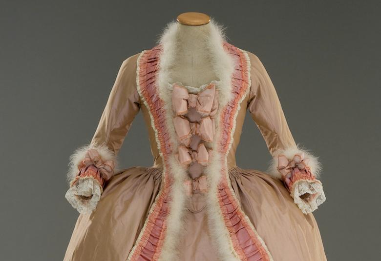 Kuvassa on Marie Antoinette -elokuvan puvun tiukka vaalean ruskea yläosa ja kaula-aukon valkoinen karvareunus sekä rosan väristä koristetta.  
