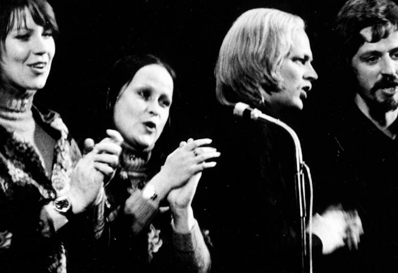 Kuvassa ovat Agit-Propin laulajan Monna Kamu, Sinikka Sokka, Pekka Aarnio ja Martti Launis laulamassa mikrofonien edessä.  Heistä on puolivartalokuvat ja kuva on musta-valkoinen.