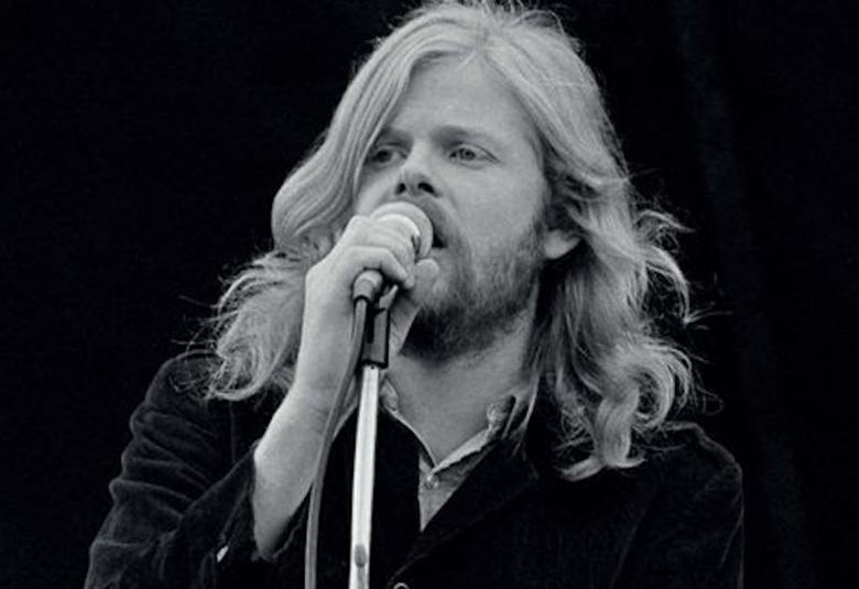 Kuvassa on Eero Raittinen esiintymässä mikin ääressä musta-valkoisessa kuvassa.