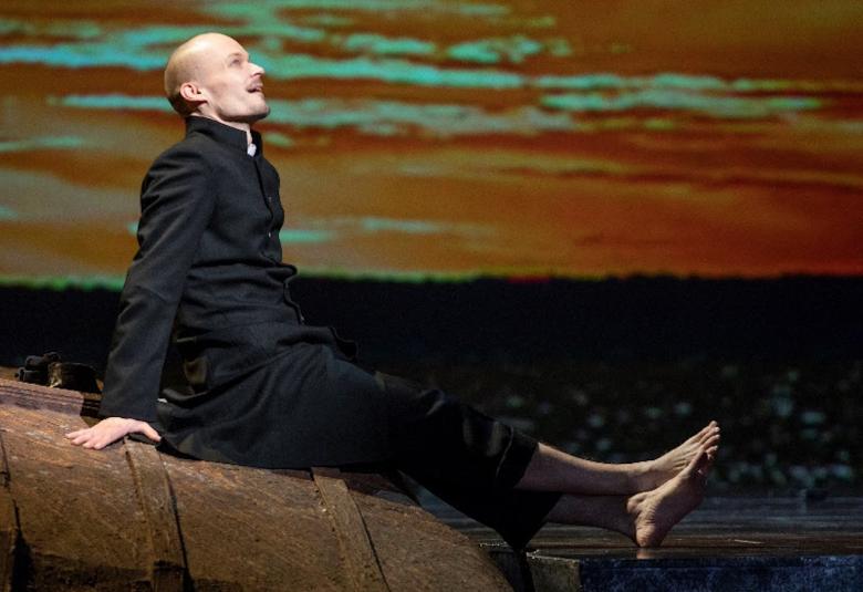 Kuvassa on Ville Rusanen sivuttain ikäänkuin kiven päällä takana iltataivas.