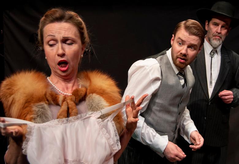 Kuvassa on anoppi, joka pitää edessään avokaulainen yöpuku ja kauhistelee sitä. Takanaan ovat miehet.