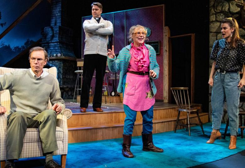 Kuvassa ollaan näyttämön olohuoneessa ja näyttämöllä on kaksi miestä ja kaksi naista. Keskellä nainen huoneen portaalla puhuu ja muut kuuntelevat.