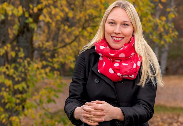 Kuvassa on Salla Ahvenjärvi istumassa ulkona vihreän pensaisto taustallaan.