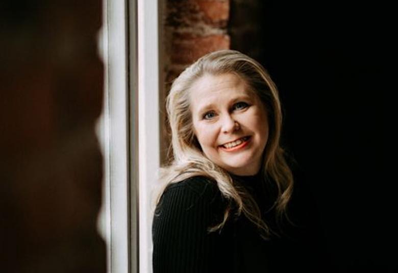 Kuvassa on Suvi Innilä puolivartalokuvassa seisomassa ikkunan ääressä. Kuvan molemmin puolin on tummaa ja ikkunasta tulee valoa.