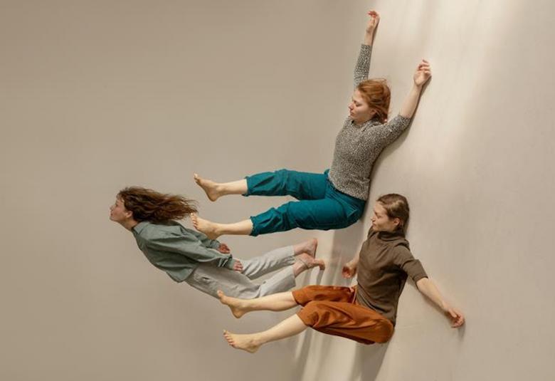 Kuvassa on kaksi tanssijaa makaamassa seinällä ja yksi seisoo seinällä. Kuvassa lattia on käännetty seinäksi.