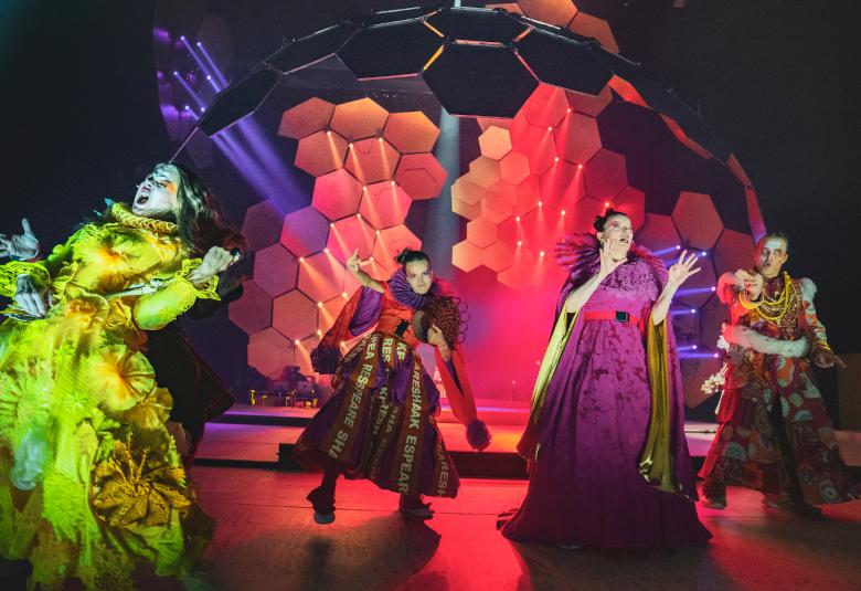 Kuvassa ovat Inke Koskinen, Maria Halinen, Petra Karjalainen, Petrus Kähkönen keltaisissa, punaisissa ja kirjavissa näyttävissä asuissa.  Takana on suuri, värikäs mehiläiskenno.