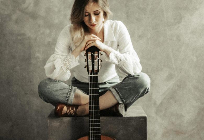 Kuvassa on Katarzyna Smolarek, joka on ristiistunnassa ja pitää kitaraa edessään ja katsoo alas.