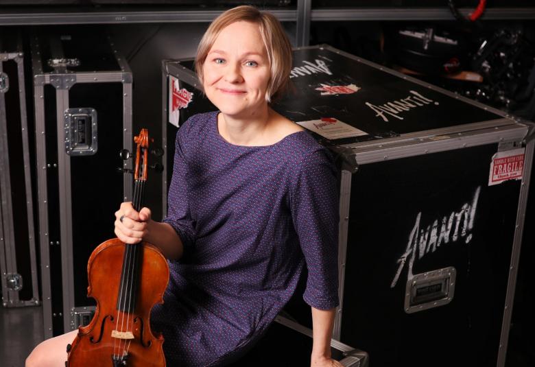 Kuvassa on Lotta Wennäkoski konserttilavan takana istumassa viulu kädessään.