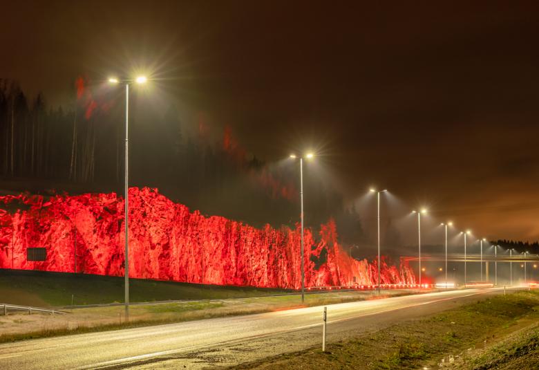 Kuvassa on Yhteys-valoteos punaisena kallioon heijastettuna.