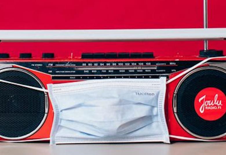 Kuvassa on punainen vanha matkaradio, jolla on edessään maski.