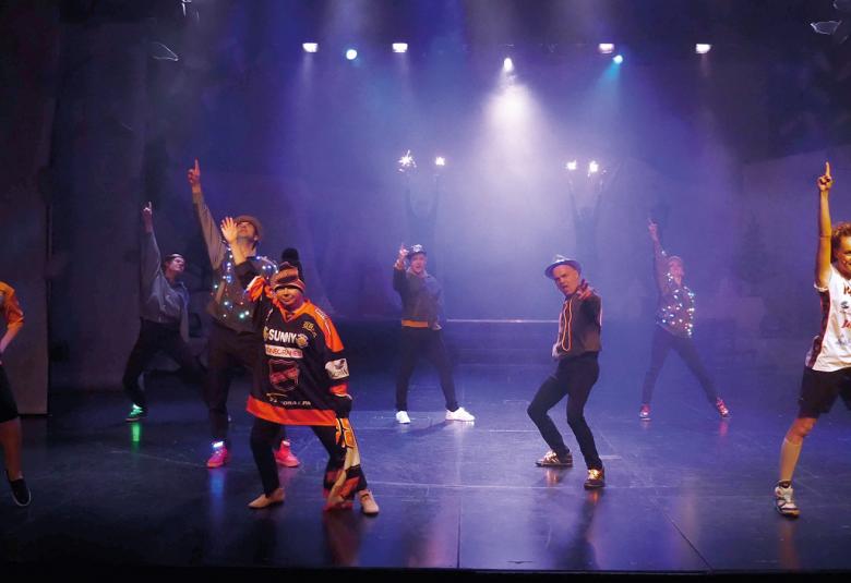  Kuvassa on koko joulushown näyttelijäkunta tanssimassa näyttämöllä. Edessä keskellä on mies Lapin puvussa.