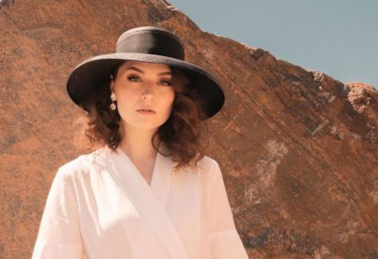 Kuvassa on Behm kuvattuna yläviistoon ja hänellä on suuri, musta lierihattu päässään.