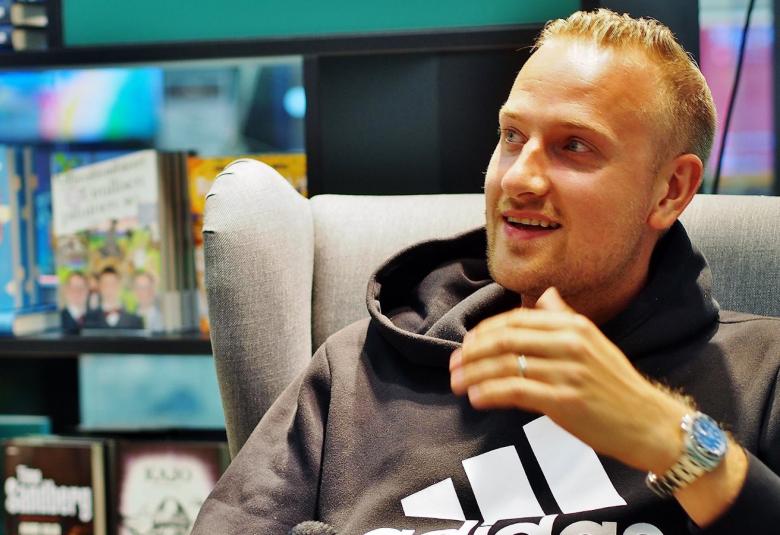 Kuvassa on Max Seeck istumassa ja kuva on otettu sivuttain.  Seeckilla on päällään college-paita.