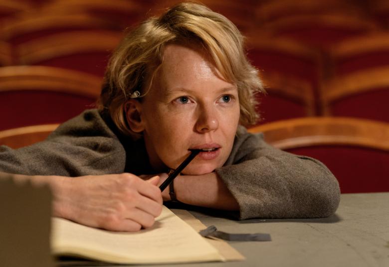 Kuvassa on Tove Janssonia esittävä Alma Pöysti nojaamassa pöytään kynä kädessään. Kuvassa näkyvät pääosin kasvot.